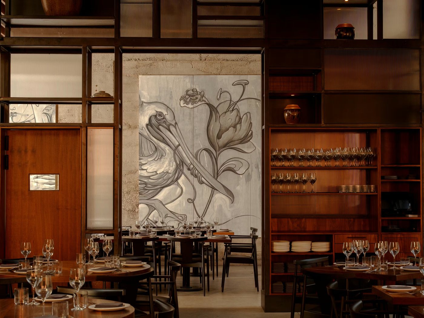 Majordomo dining room with dark wood tables and wine glasses beneath a large illustrated mural of a pelican and a lotus flower