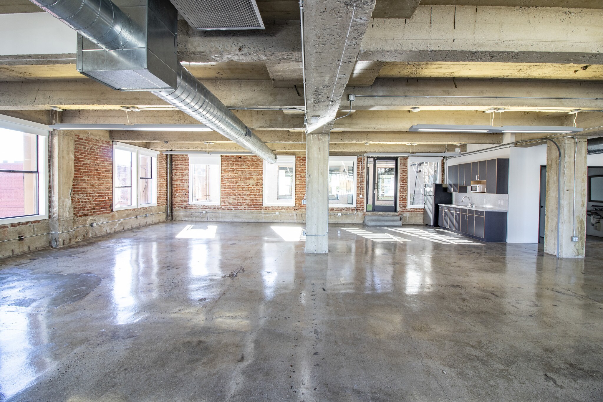 Second-floor creative office interior with exposed brick, board-formed concrete beams and polished floors